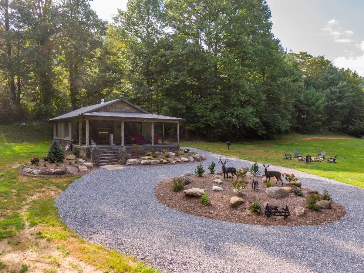 A welcoming view of the house showing an inviting porch, a decorative rock garden, and a cozy seating area with chairs. The landscaping blends seamlessly with the surrounding nature, suggesting easy transitions between indoor comfort and outdoor adventure.