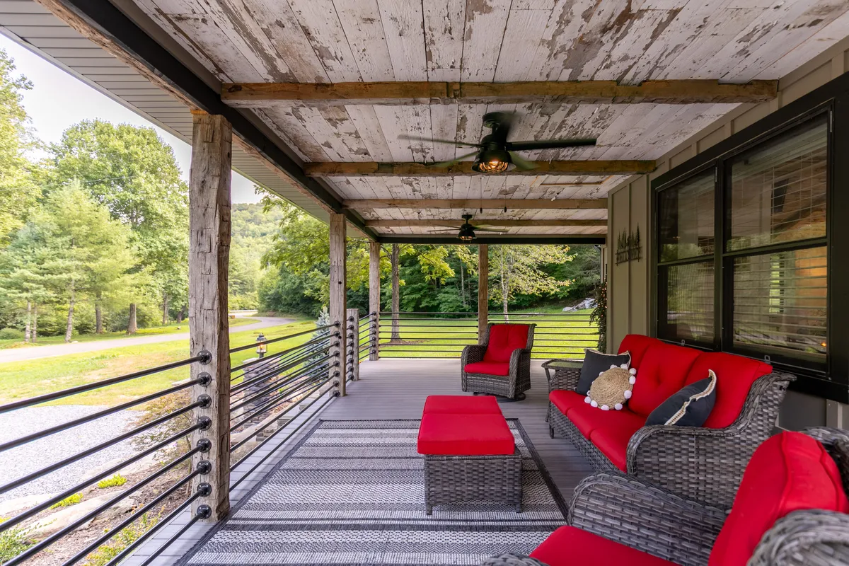 This image shows another angle of the covered deck, highlighting its wooden beams, comfortable seating adorned with red cushions, and a backdrop of lush green trees. The overhead ceiling fans add to the sense of relaxation, while the expansive views hint at the deck's wrap-around design.
