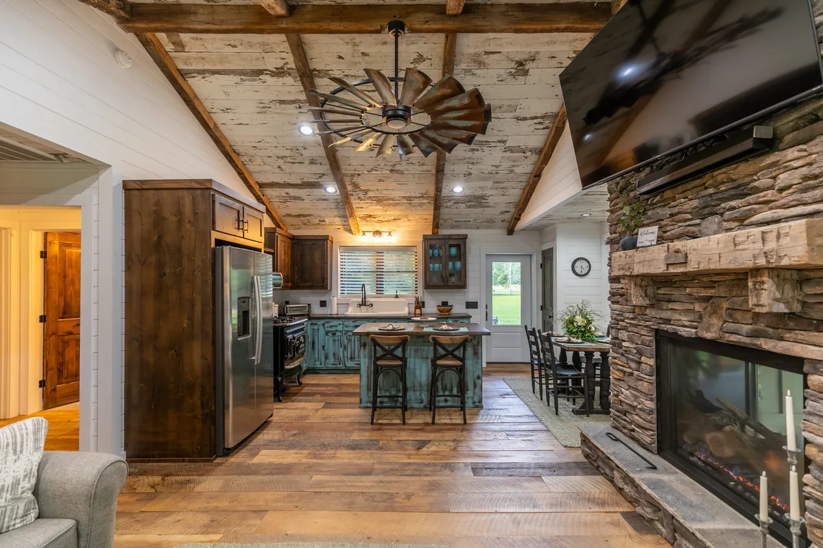Inside, a modern kitchen with a spacious island, stone fireplace, and large windows is featured. The warm, inviting space is ideal for family cooking, entertaining, and cozying up by the fire after outdoor adventures.
