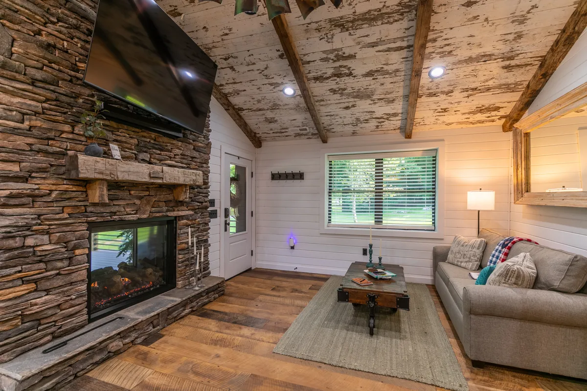 This image captures a plush sofa set in front of a stone fireplace with a TV mounted above it. The coffee table and a view of the outdoors through the window create an inviting, communal space perfect for relaxing or socializing. The warm tones and arrangement encourage group activities and comfort.