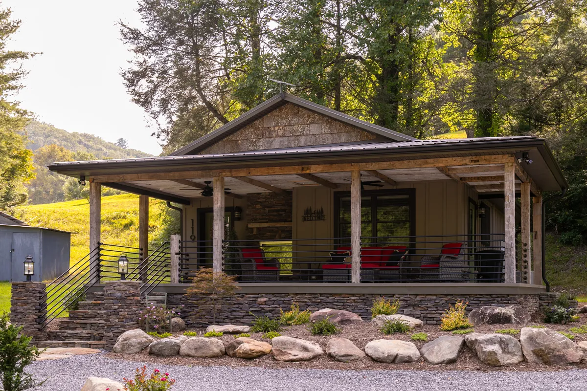 A cozy front porch with red chairs overlooks stone landscaping and lush greenery. Wooden supports and railings enhance the rustic charm, while the porch itself offers a perfect vantage point for enjoying sunsets or morning coffee with nature all around.