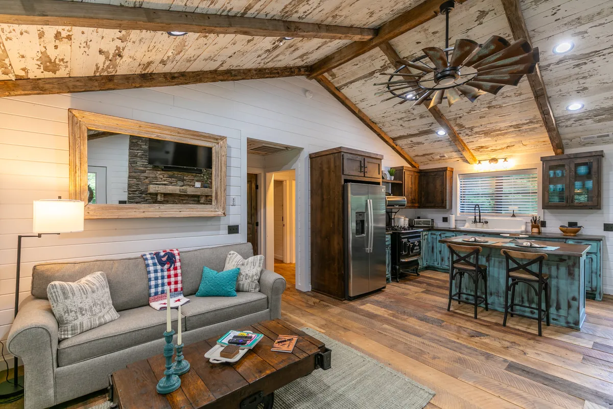 A wide, open-plan view featuring a welcoming sofa, coffee table, kitchen island, and ceiling fan. The arrangement suggests a seamless flow between living and kitchen areas, with ample space for relaxation, entertaining, and connection. The mirror reflects light, enhancing the inviting atmosphere.