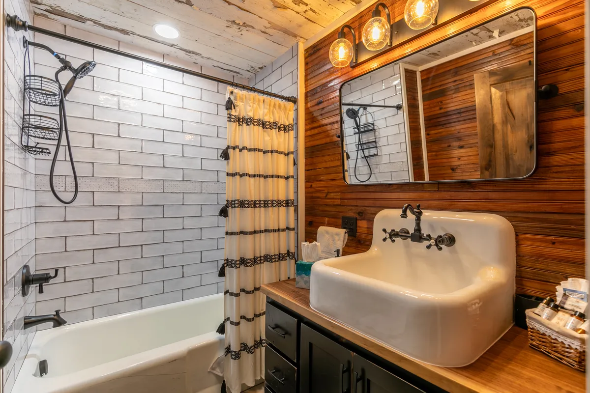 A beautifully appointed bathroom featuring a freestanding bathtub, vintage farmhouse-style sink, elegant wooden accent wall, and stylish light fixtures. The space exudes a spa-like calm, inviting relaxation and rejuvenation.