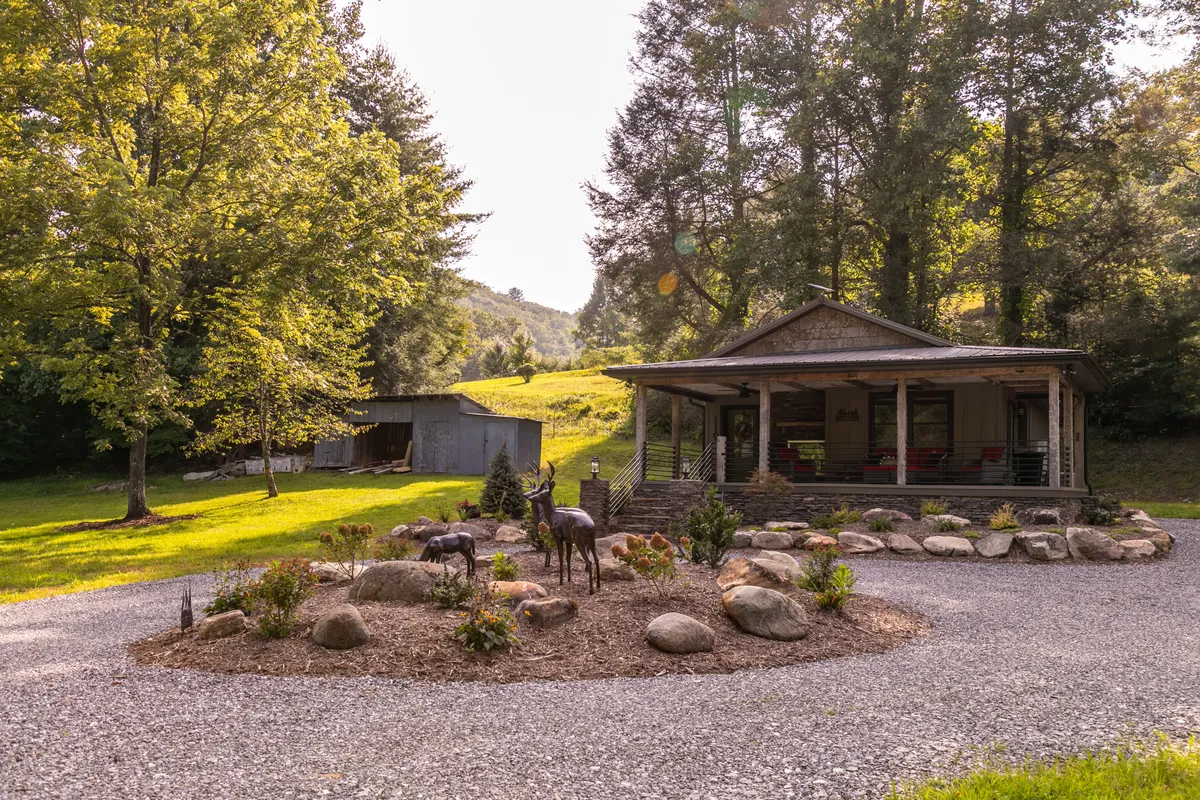 This image features the exterior of the house, surrounded by a welcoming garden, a gravel pathway, and decorative deer sculptures. The porch offers a view for relaxation, and the lush landscaping highlights the property's connection to nature and the serene mountain environment.