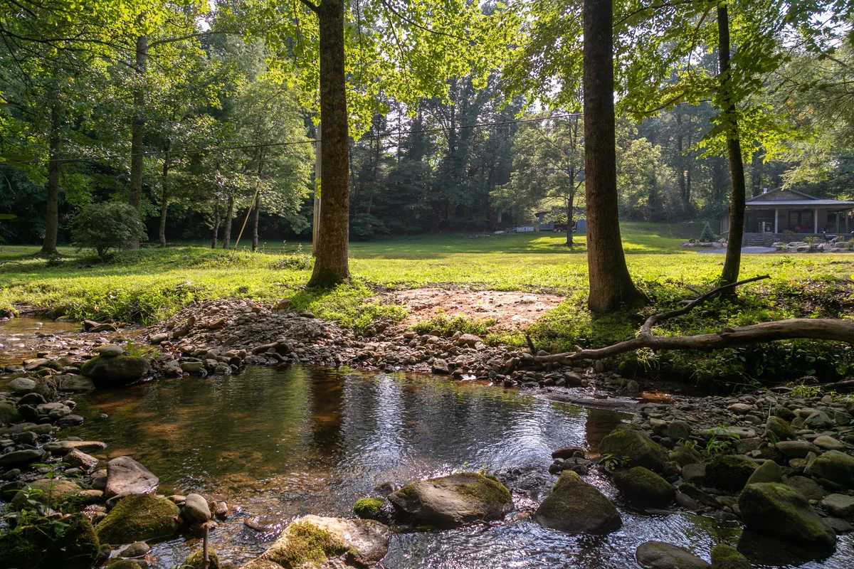 A peaceful creek flows through lush greenery, with a distant gazebo adding a touch of charm. The tranquil waters and surrounding foliage evoke a sense of privacy and connection to the outdoors, perfect for picnicking, nature walks, or quiet reflection.